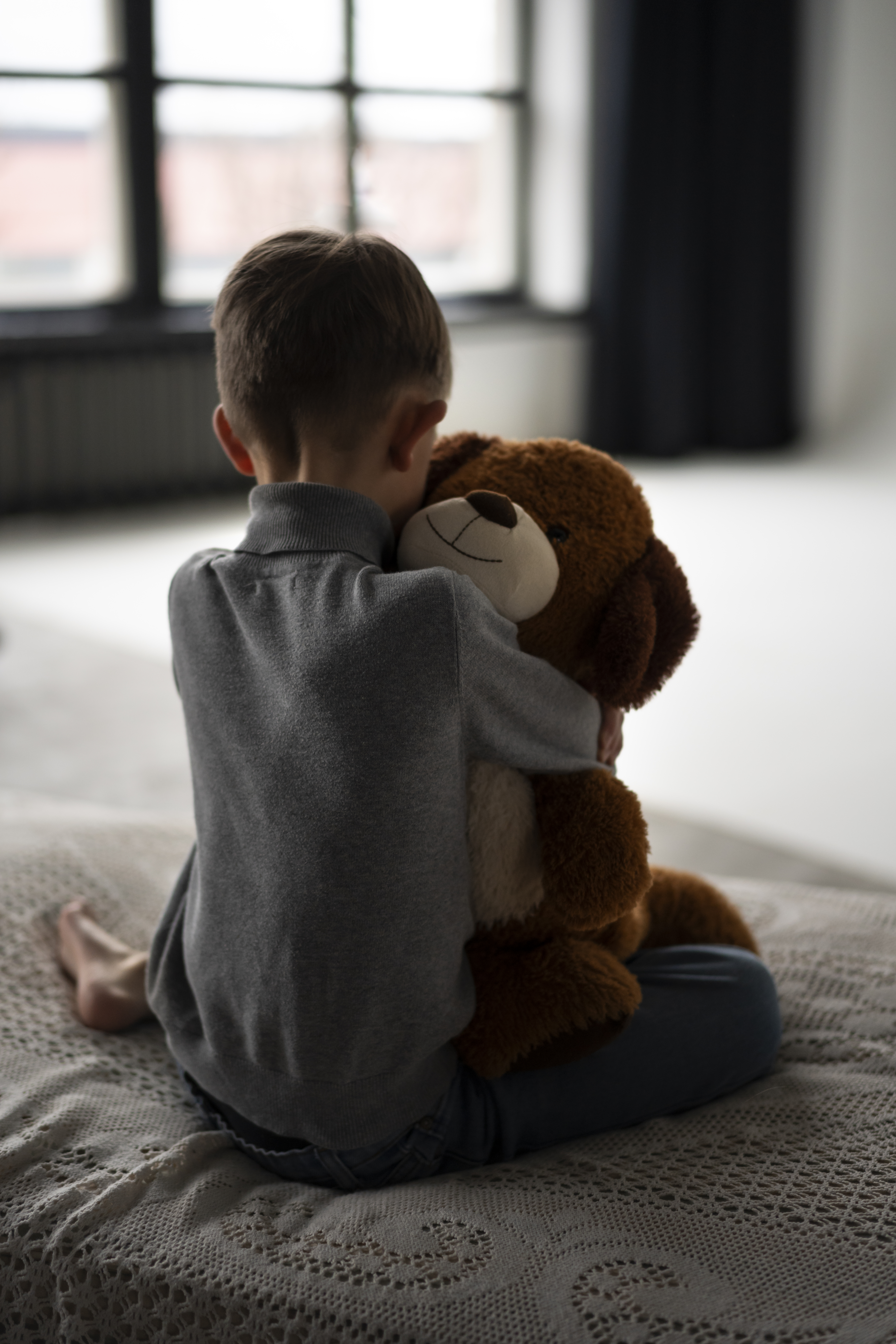 niño sentado en la cama abrazando a un oso de peluche